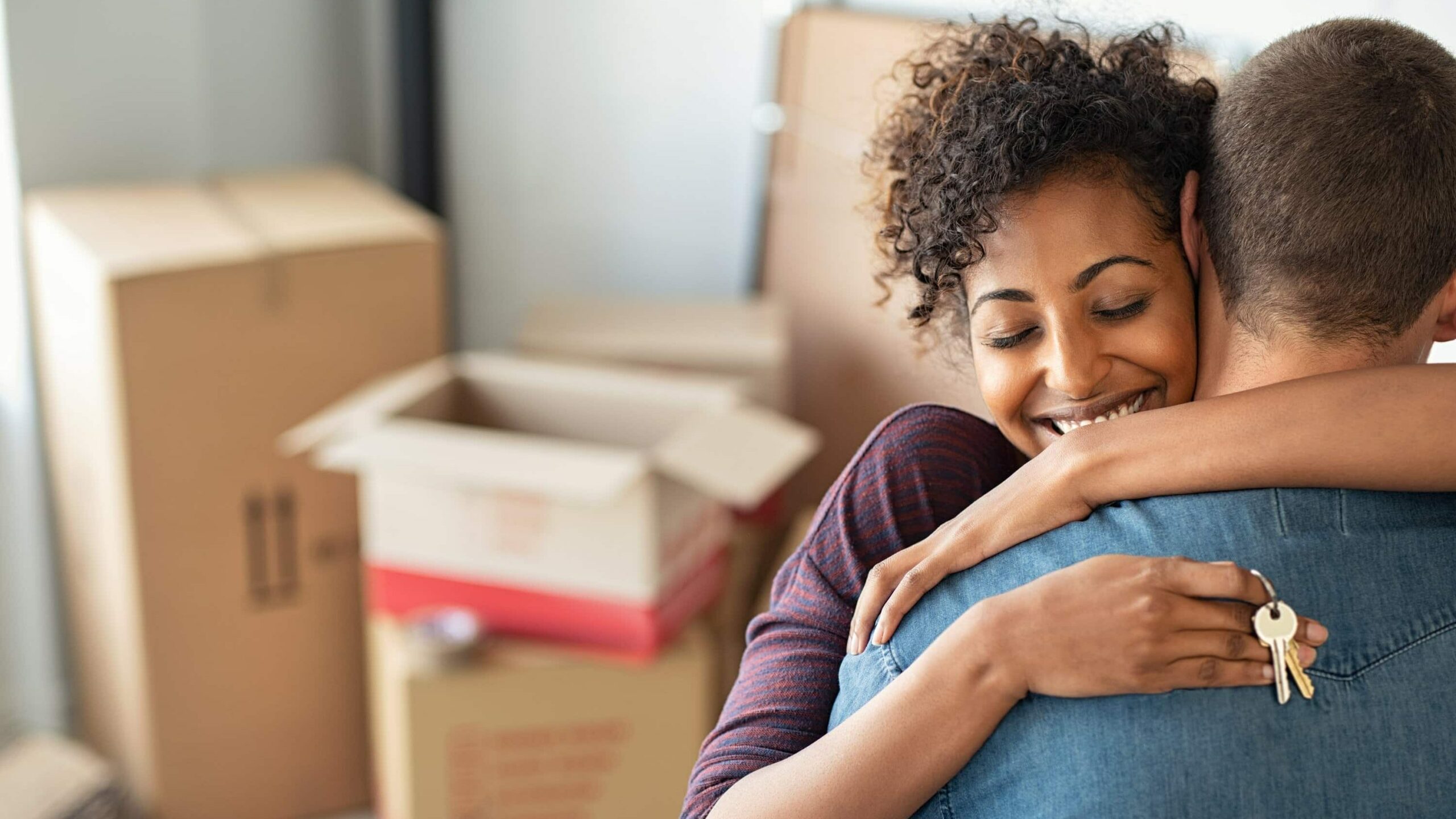 Young couple hugging whilst unpacking boxes - find Shared Ownership homes on Share to Buy!