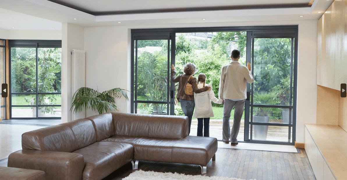Family stand by large glass doors, looking out at the garden. Start your search for a new home on Share to Buy!