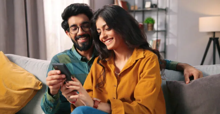 couple holding and smiling at a phone sat on the sofa