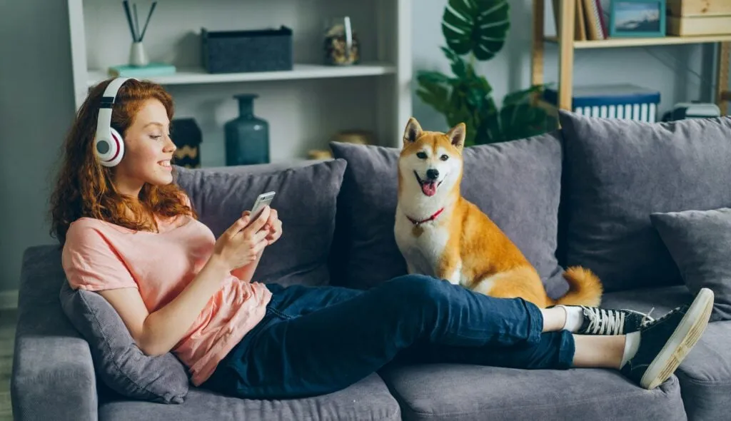 woman listening to music with headphones on sofa with dog