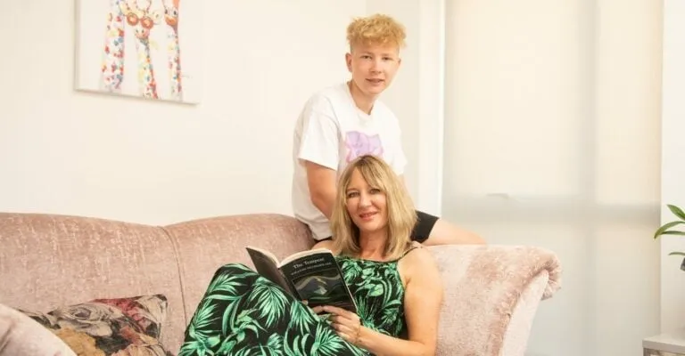 mum sat on the sofa reading a book with son leaning on the arm of sofa