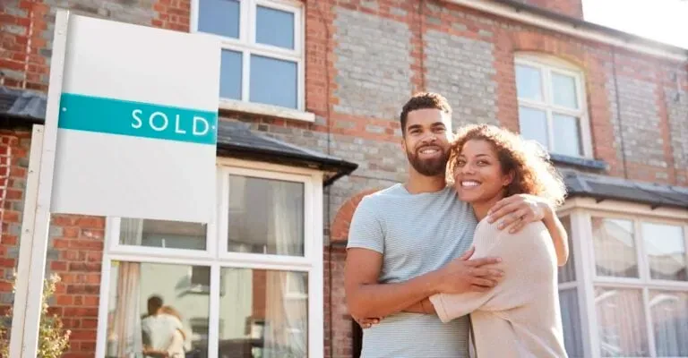 couple hugging infront of sold house sign