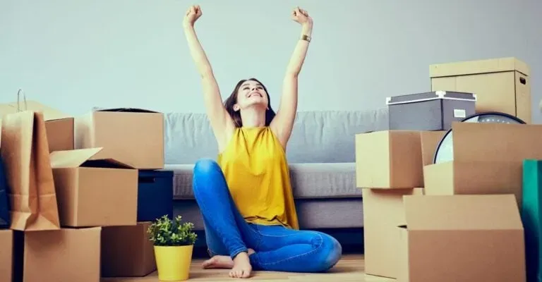 woman sitting on the floor surrounded by boxes celebrating