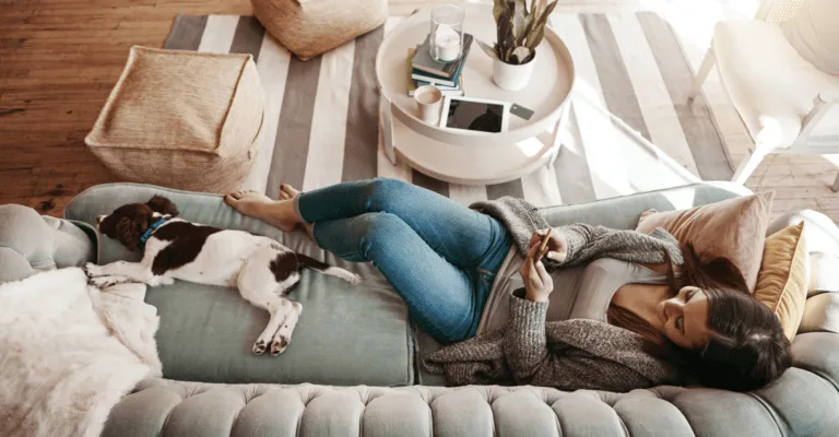 woman sat on sofa on her phone with dog laid out