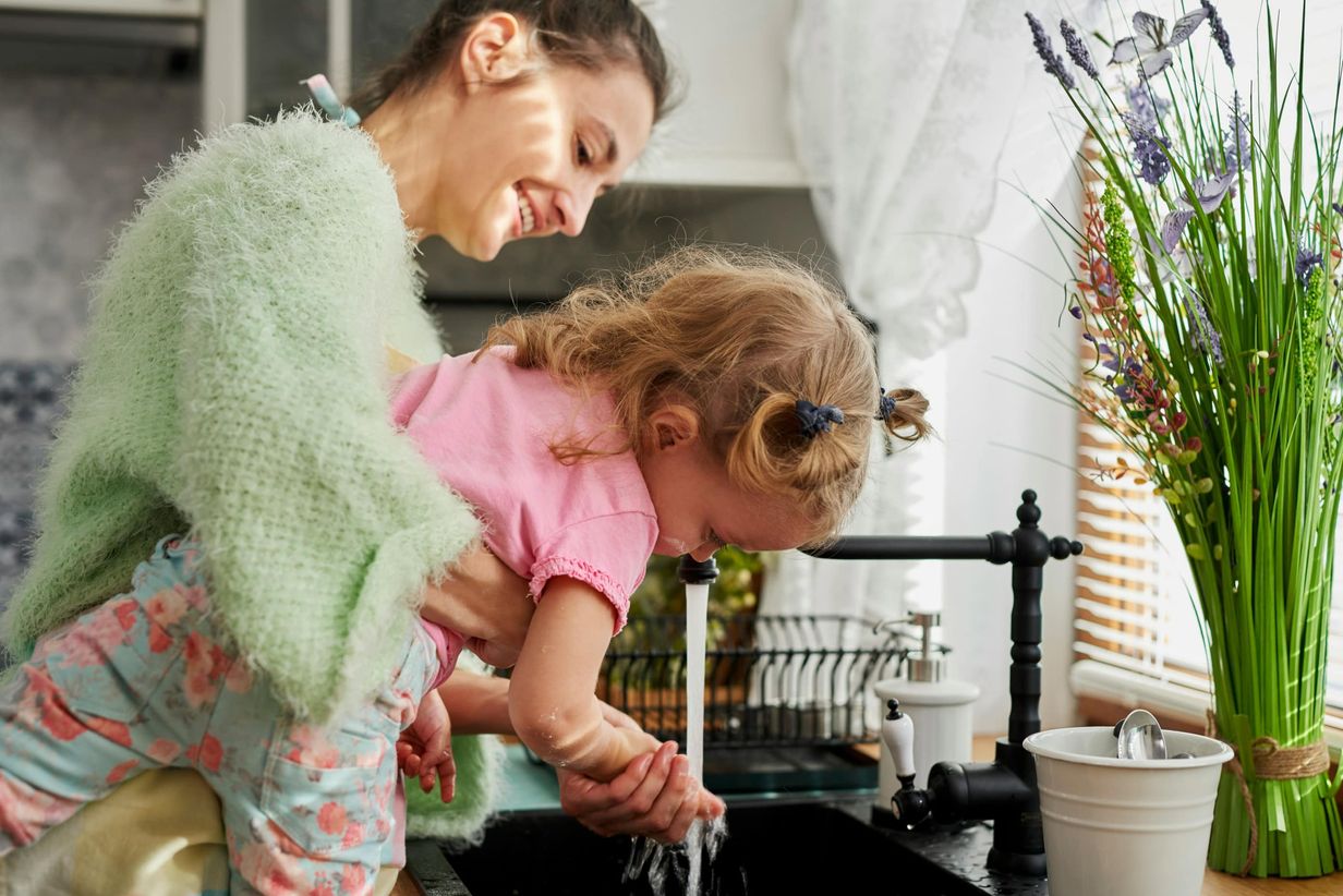 A mother washing her daughter's hands in their kitchen.