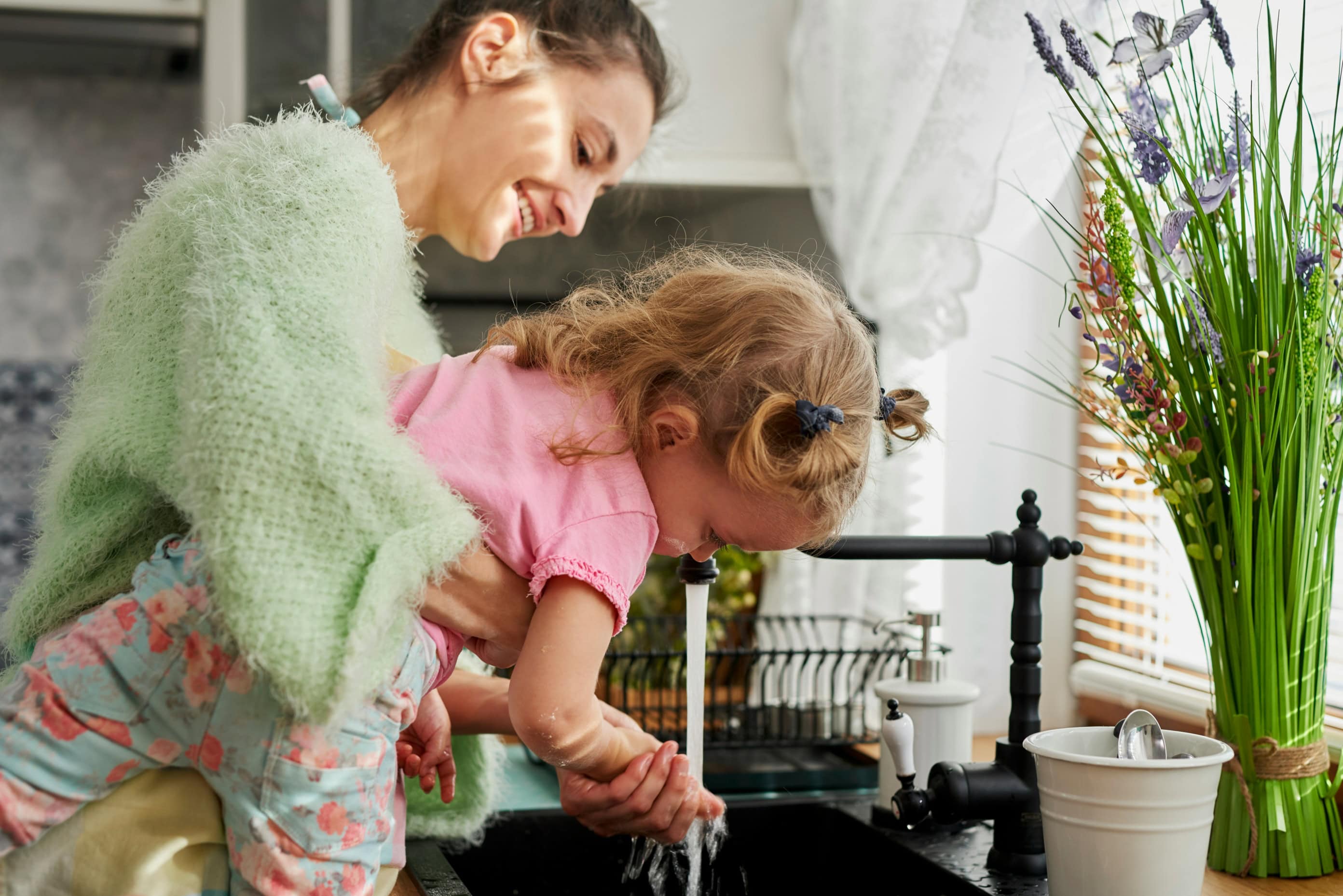 A mother washing her daughter's hands in their kitchen.